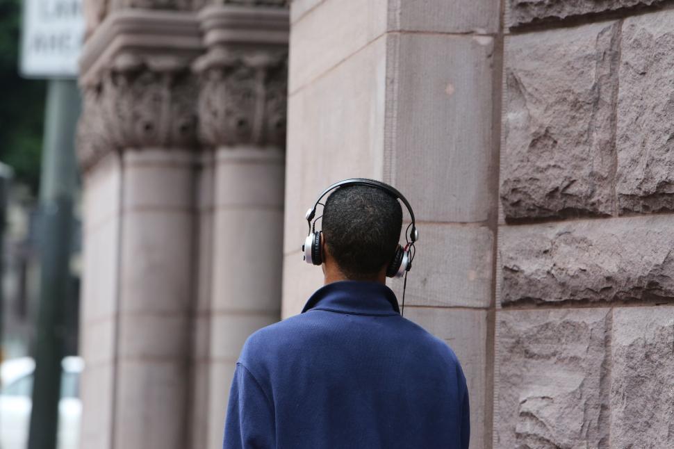 Free Image of Person with headphones walking by stone building in urban setting 