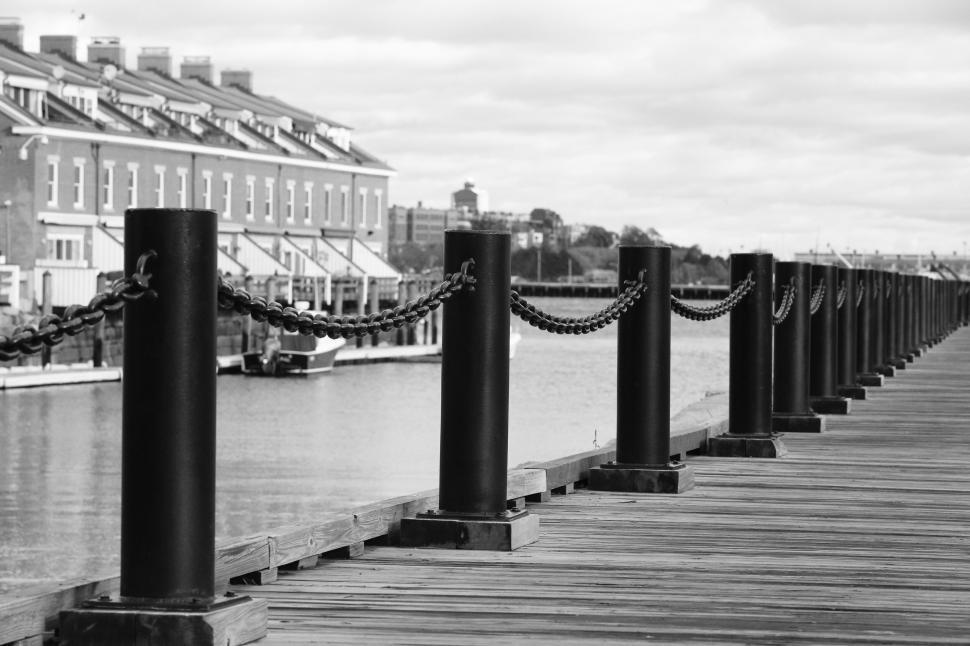 Free Image of Chain fence along a wooden pier with buildings in background 