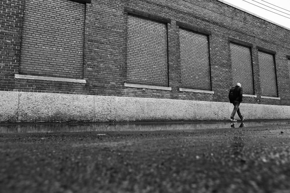 Free Image of Person walks along brick building sidewalk on a rainy day in city 