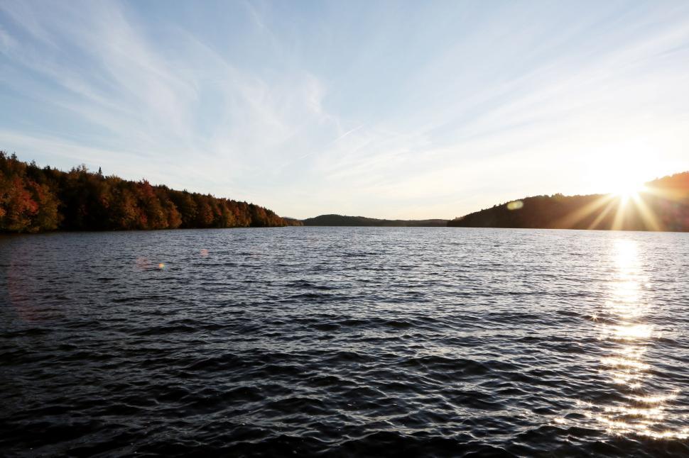 Free Image of Sunset over a calm lake surrounded by autumnal forest landscape. 