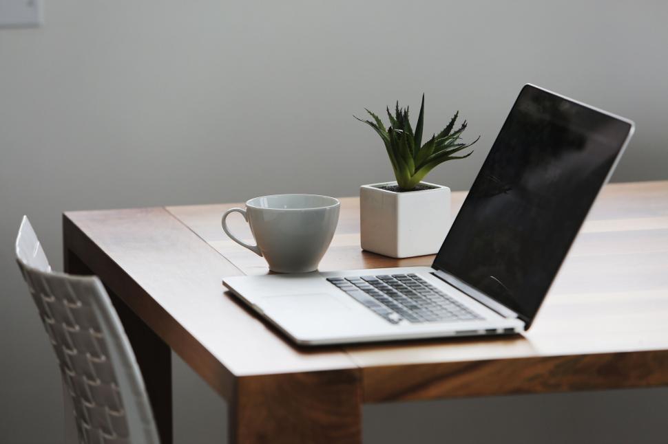 Free Image of Laptop, coffee cup, and plant on a wooden table for workspace setup. 