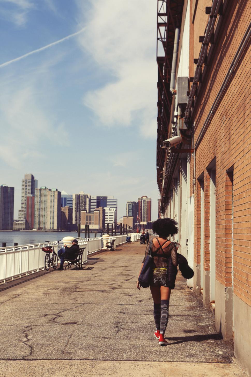 Free Image of Woman walking along urban waterfront with cityscape background view 