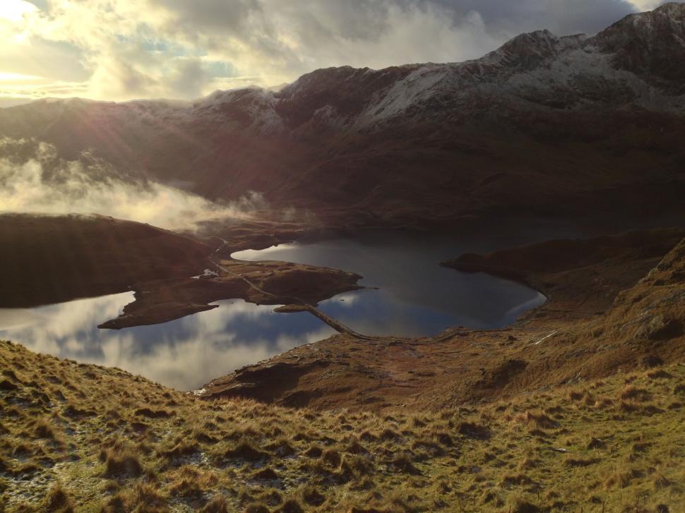 Free Image of Sunset over serene lake surrounded by mountains and rolling hills. 