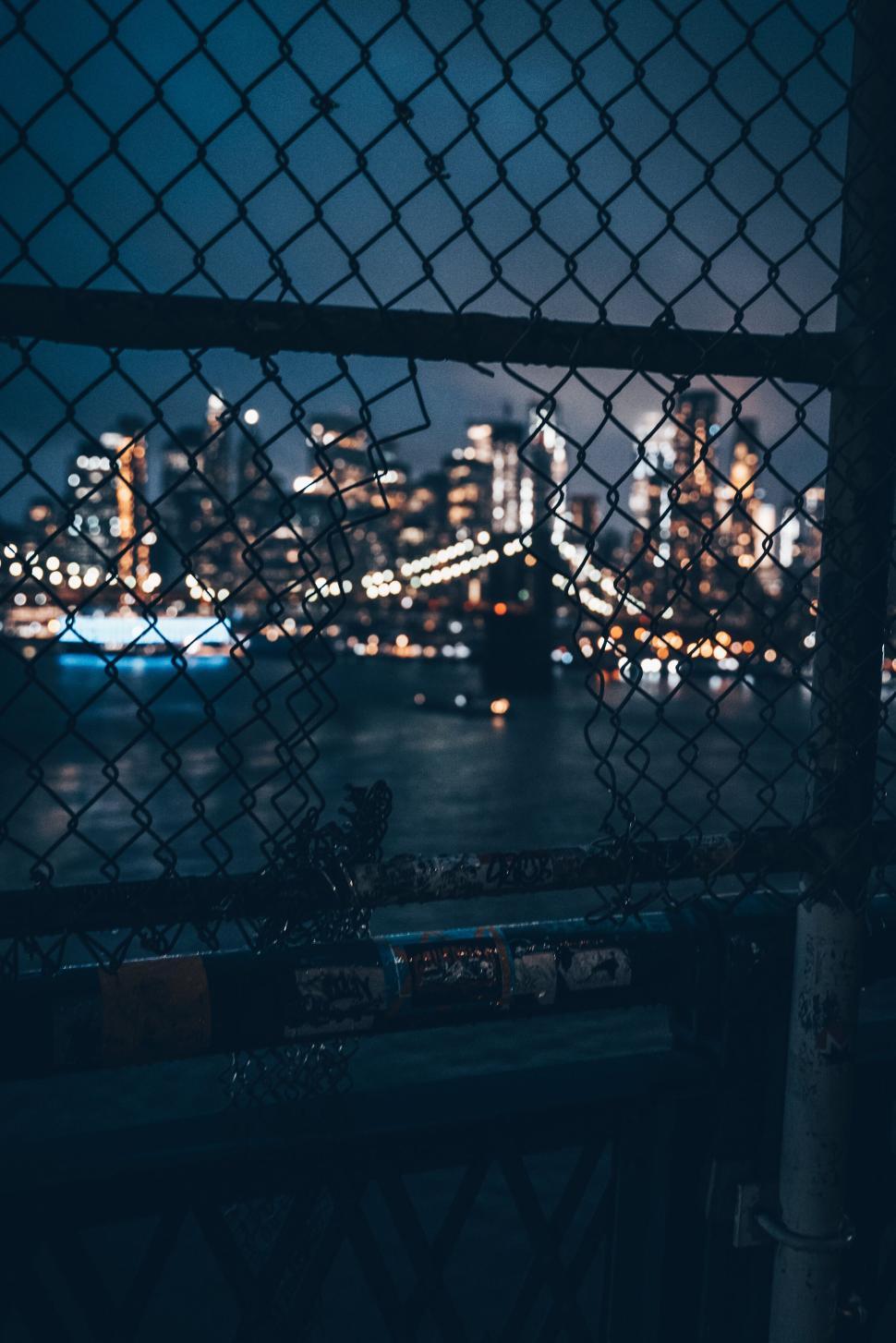 Free Image of Cityscape through a fence at night with sparkling bridge lights. 