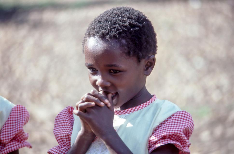 Free Image of Young girl with hands clasped wearing red gingham dress outdoors. 