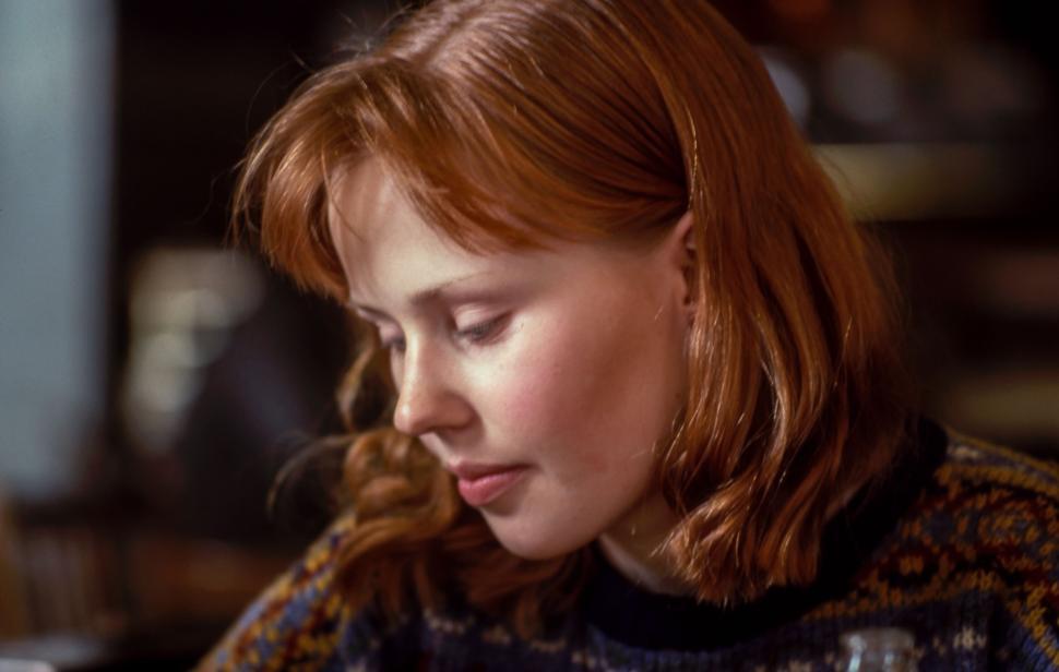 Free Image of Young woman with red hair looking down, wearing casual sweater. 