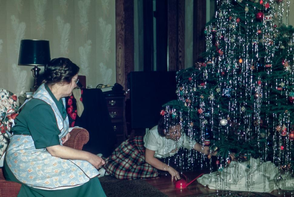 Free Image of Two women decorate tinsel-covered Christmas tree in cozy living room. 