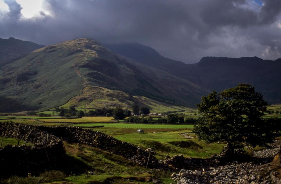 Free Image of Scenic landscape with rolling hills and stone walls under cloudy sky 
