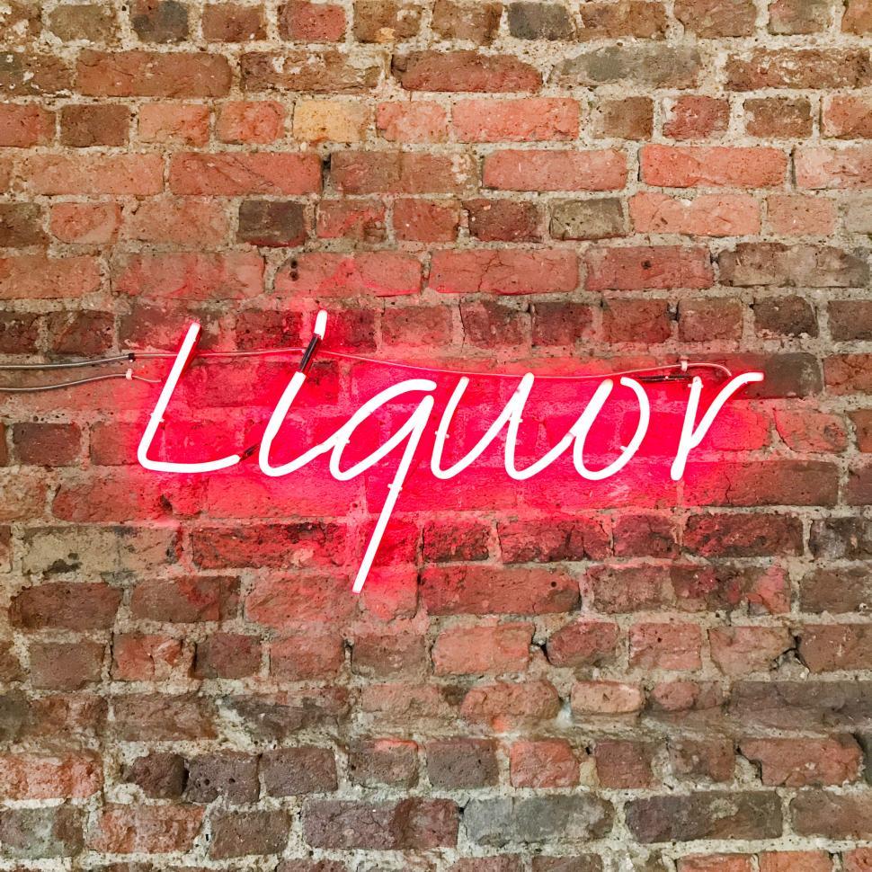Free Image of Neon red liquor sign glowing against a brick wall in urban setting 