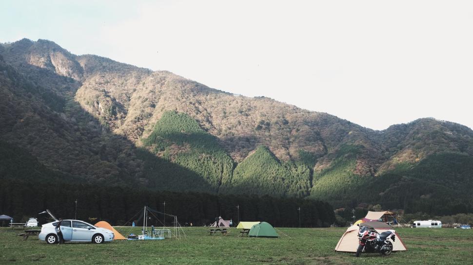 Free Image of Campsite with tents, car, and motorcycle against mountain backdrop 