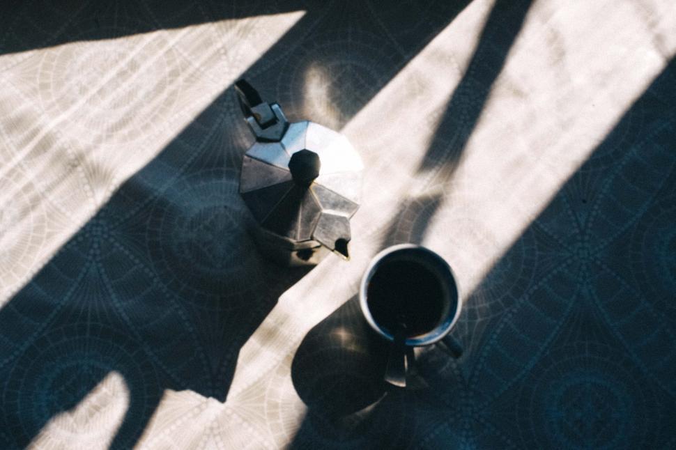 Free Image of Moka pot and cup of coffee bathed in sunlight on patterned tabletop 