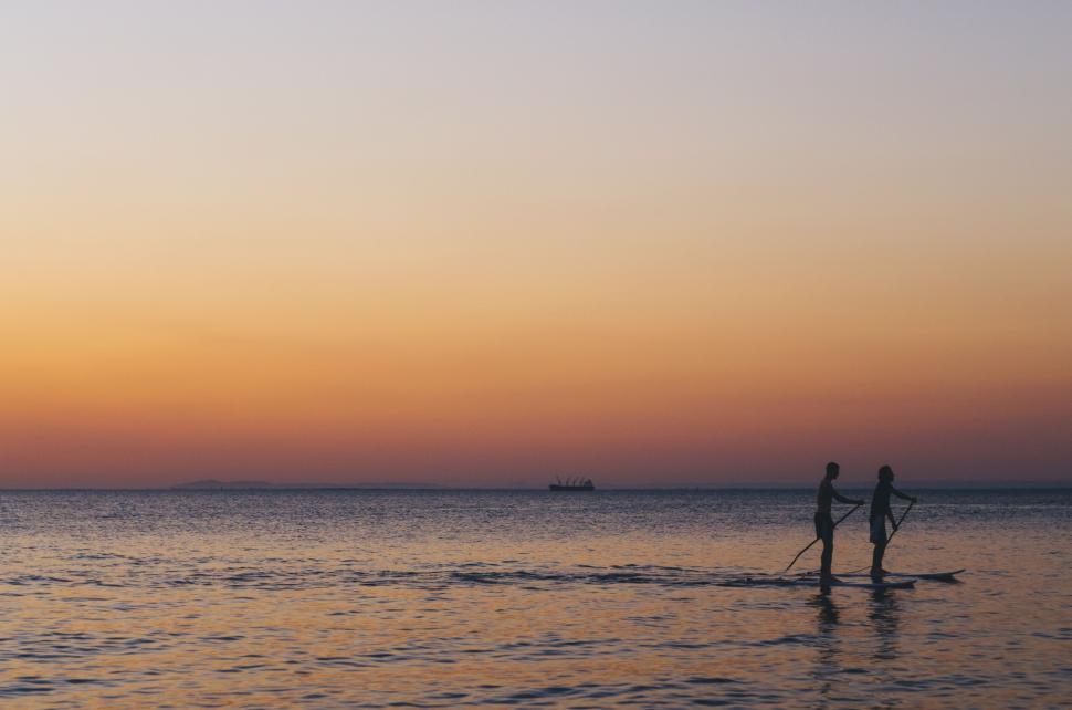 Free Image of Silhouetted paddleboarders at sunset on calm sea waters 