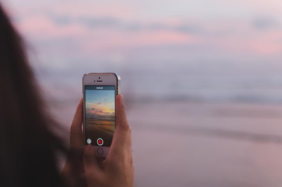 Free Image of Person photographing a beach sunset with their smartphone in focus 