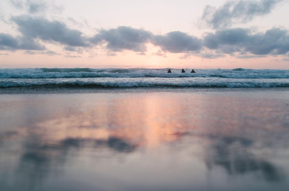 Free Image of Serene beach at dusk with gentle waves and distant figures in water 
