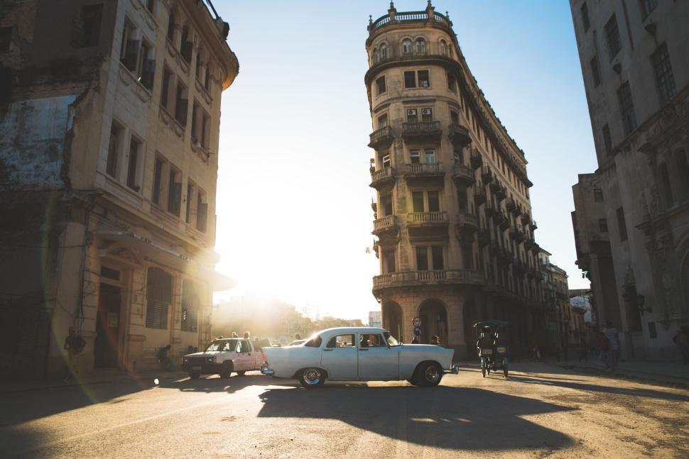 Free Image of Vintage car driving past historic building in sunlit urban setting. 