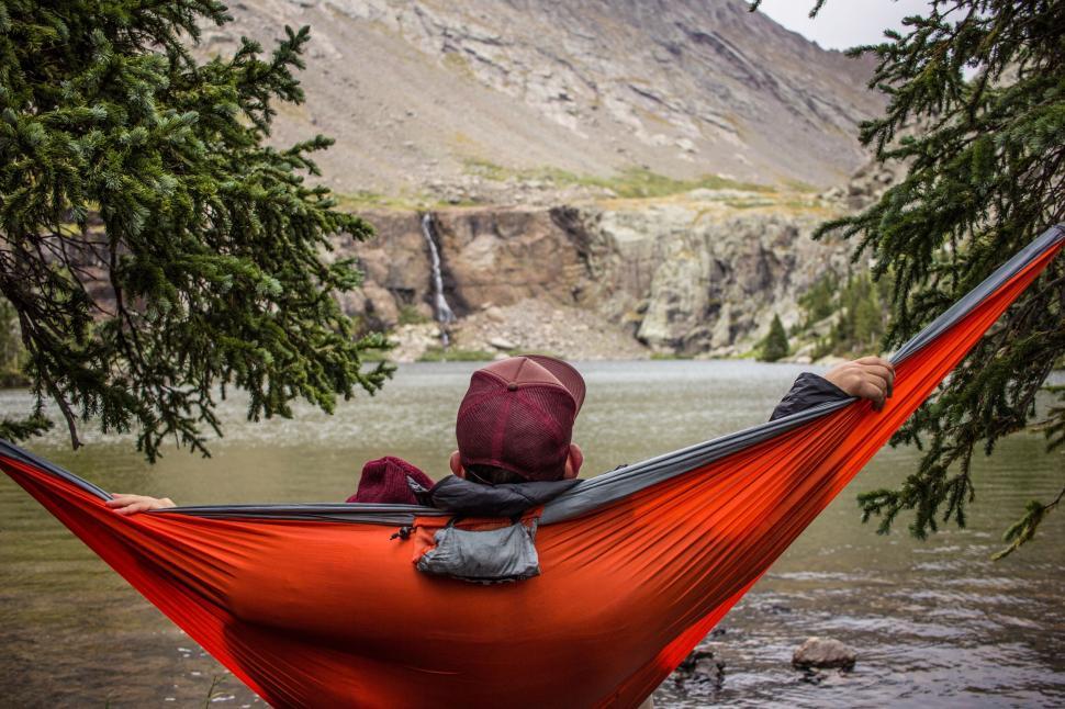 Free Image of Person relaxing on a hammock facing a serene mountain lake 