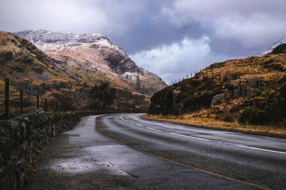 Free Image of Winding road leading through mountainous landscape with cloudy sky. 
