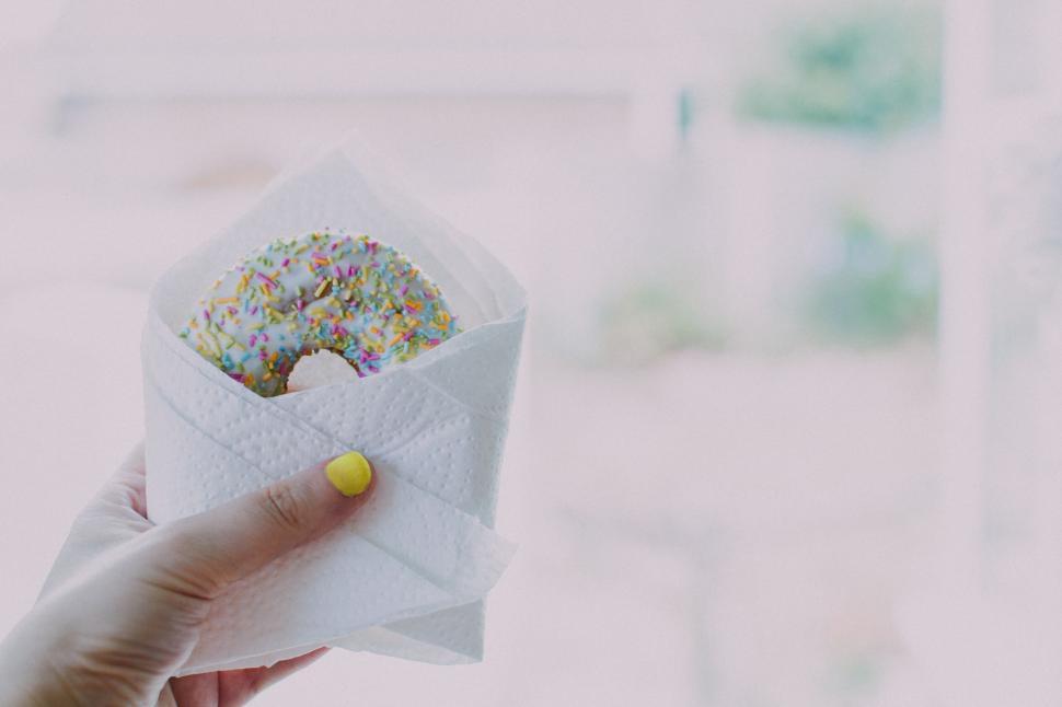 Free Image of Close-up of a donut with colorful sprinkles held by a hand 