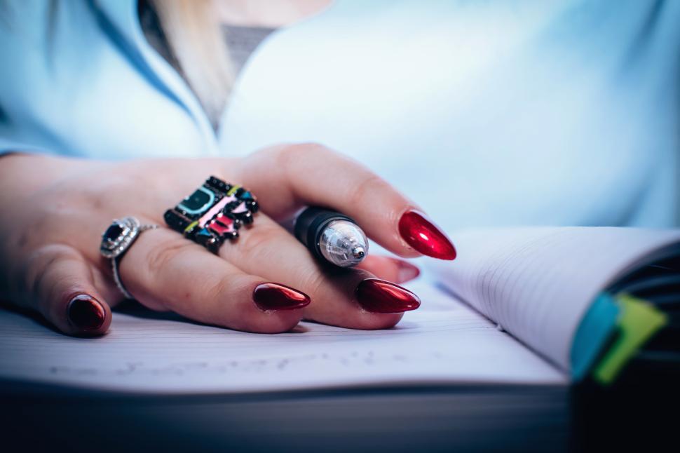Free Image of Hand with red nail polish writing in a notebook holding a black pen. 
