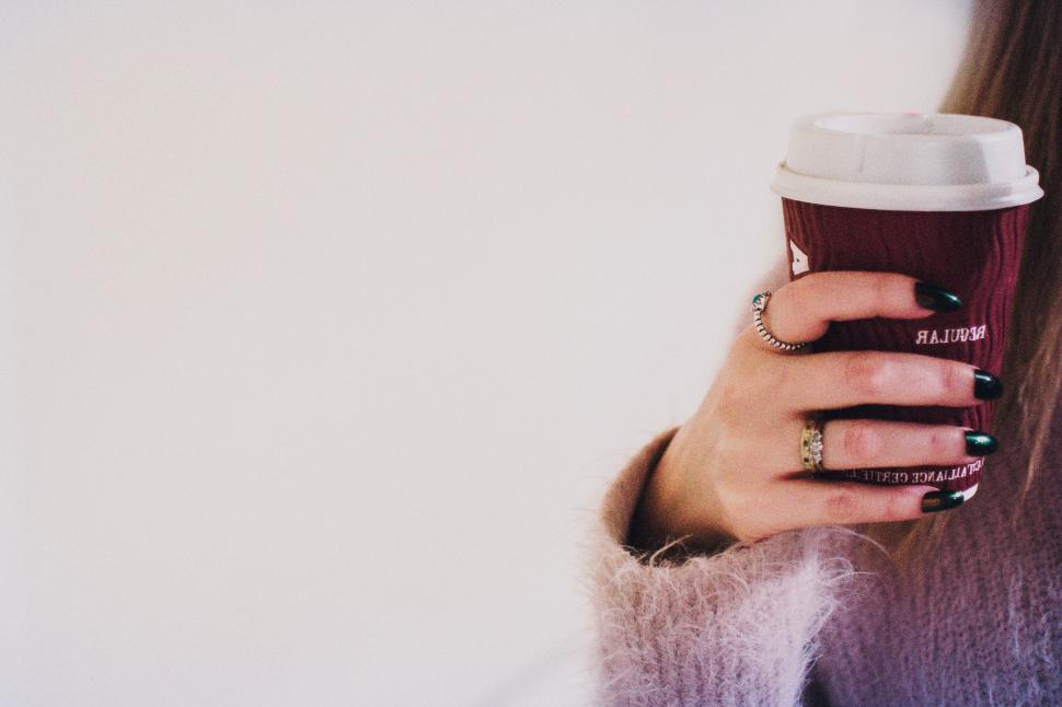 Free Image of Hand holding a takeaway coffee cup with a ring on the finger. 