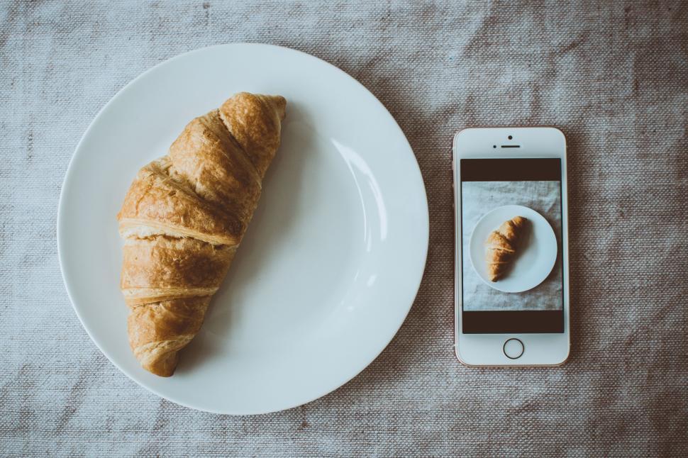 Free Image of Baked croissant on a white plate next to a smartphone photograph 