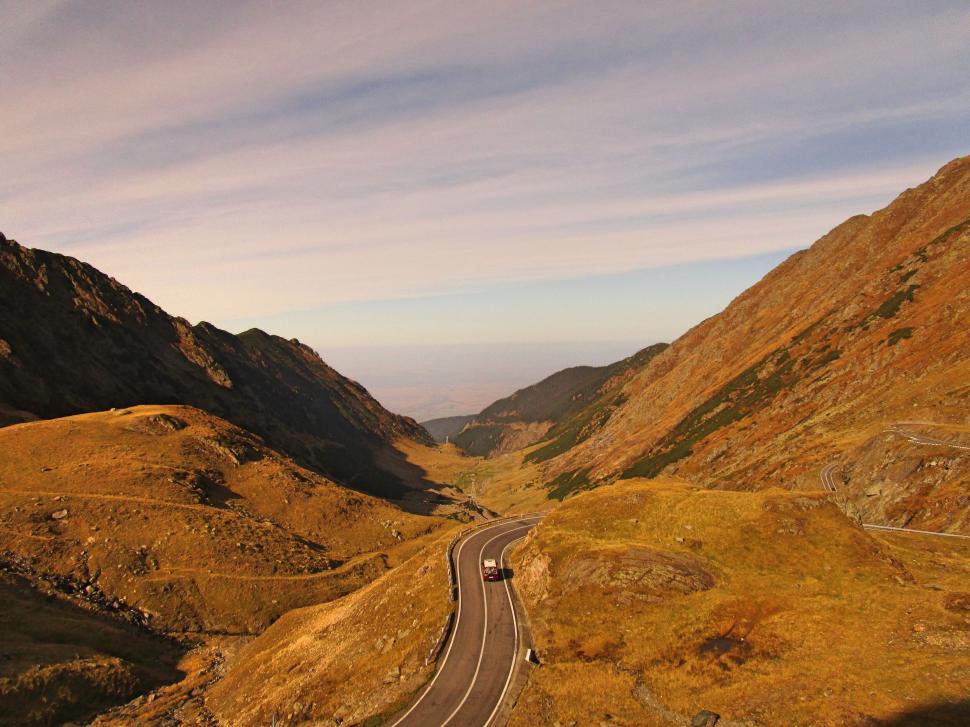 Free Image of A beautiful mountainous landscape with a winding road under a serene sky. 