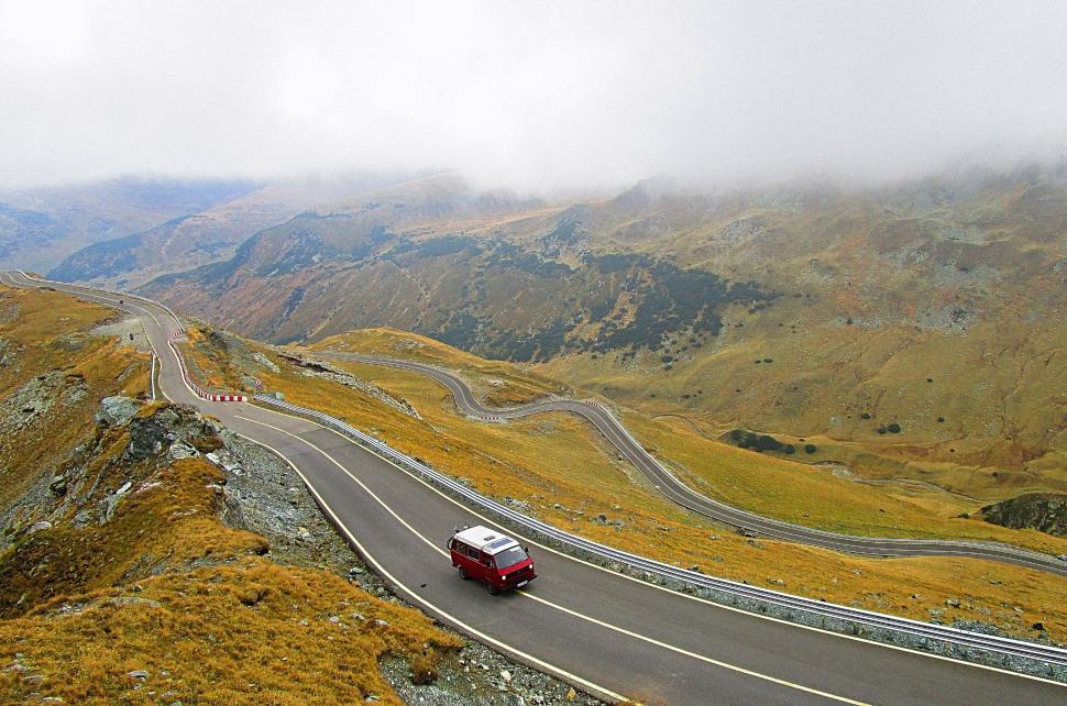 Free Image of Red van driving down curvy mountain road with scenic landscape view 