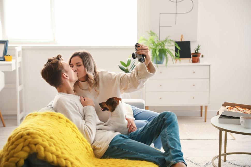 Free Image of Couple kissing on couch, capturing moment with camera, cozy home. 