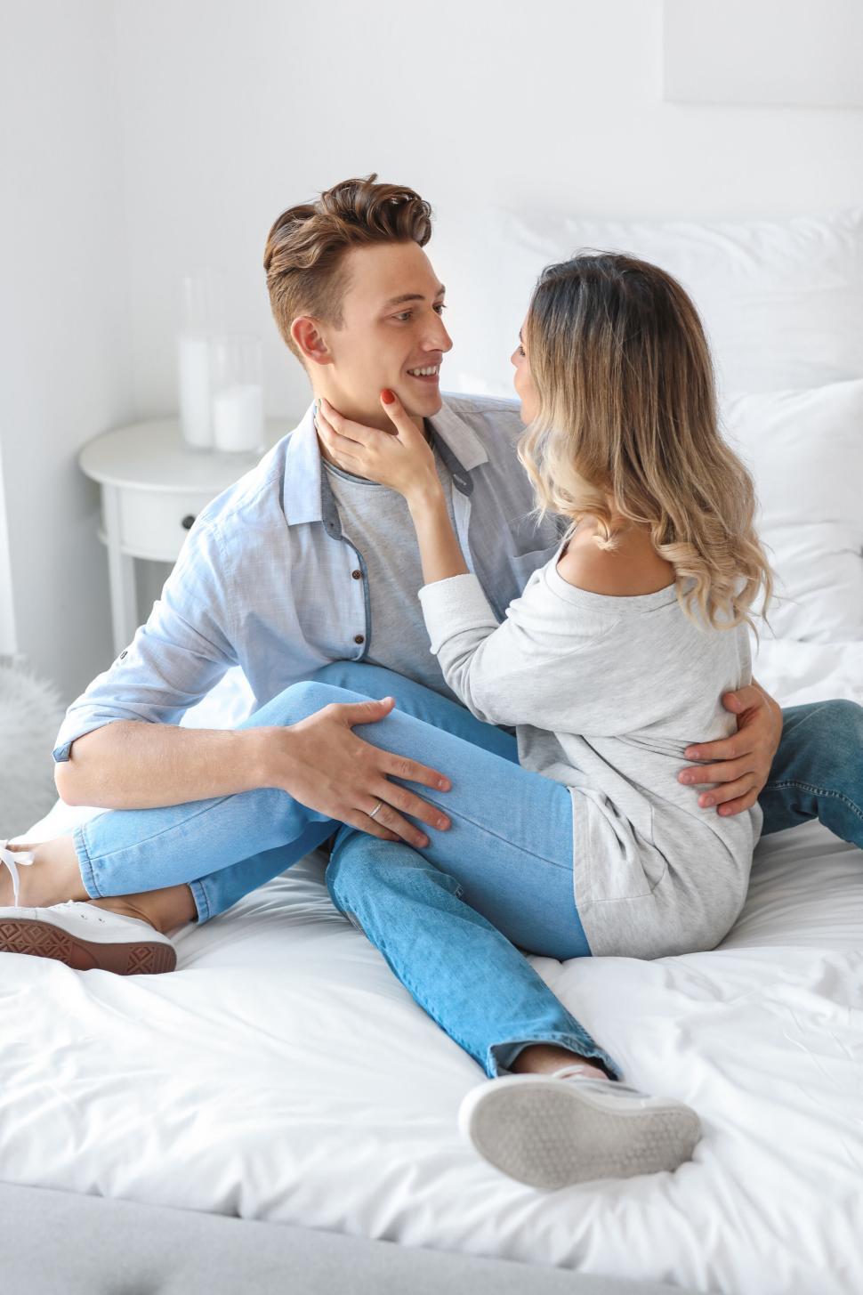 Free Image of Couple lovingly embracing on a bed in a bright white bedroom 