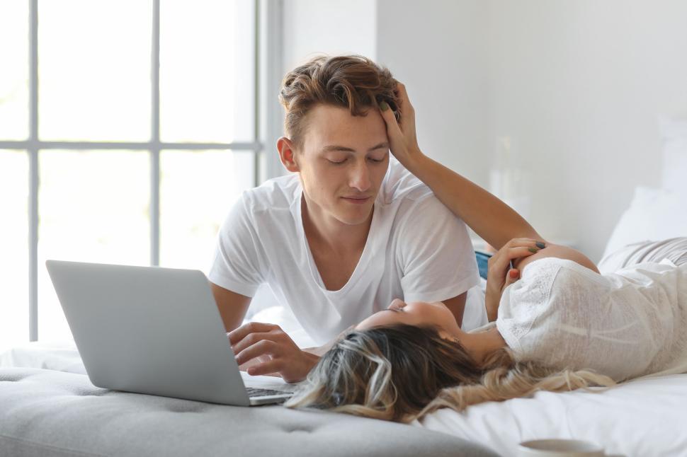 Free Image of Couple relaxing with a laptop on the bed in a bright bedroom 