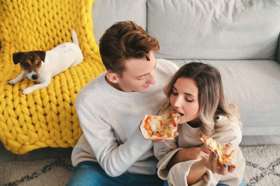 Free Image of Couple sharing pizza while sitting on the floor with dog watching 