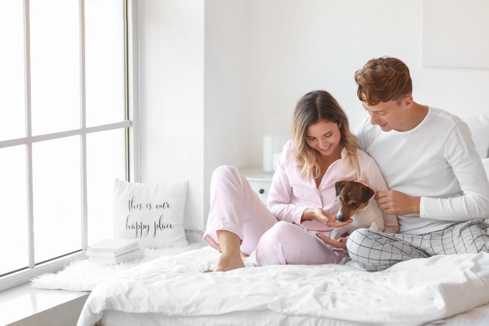 Free Image of Couple admiring their dog on bed while sharing a light-hearted moment 