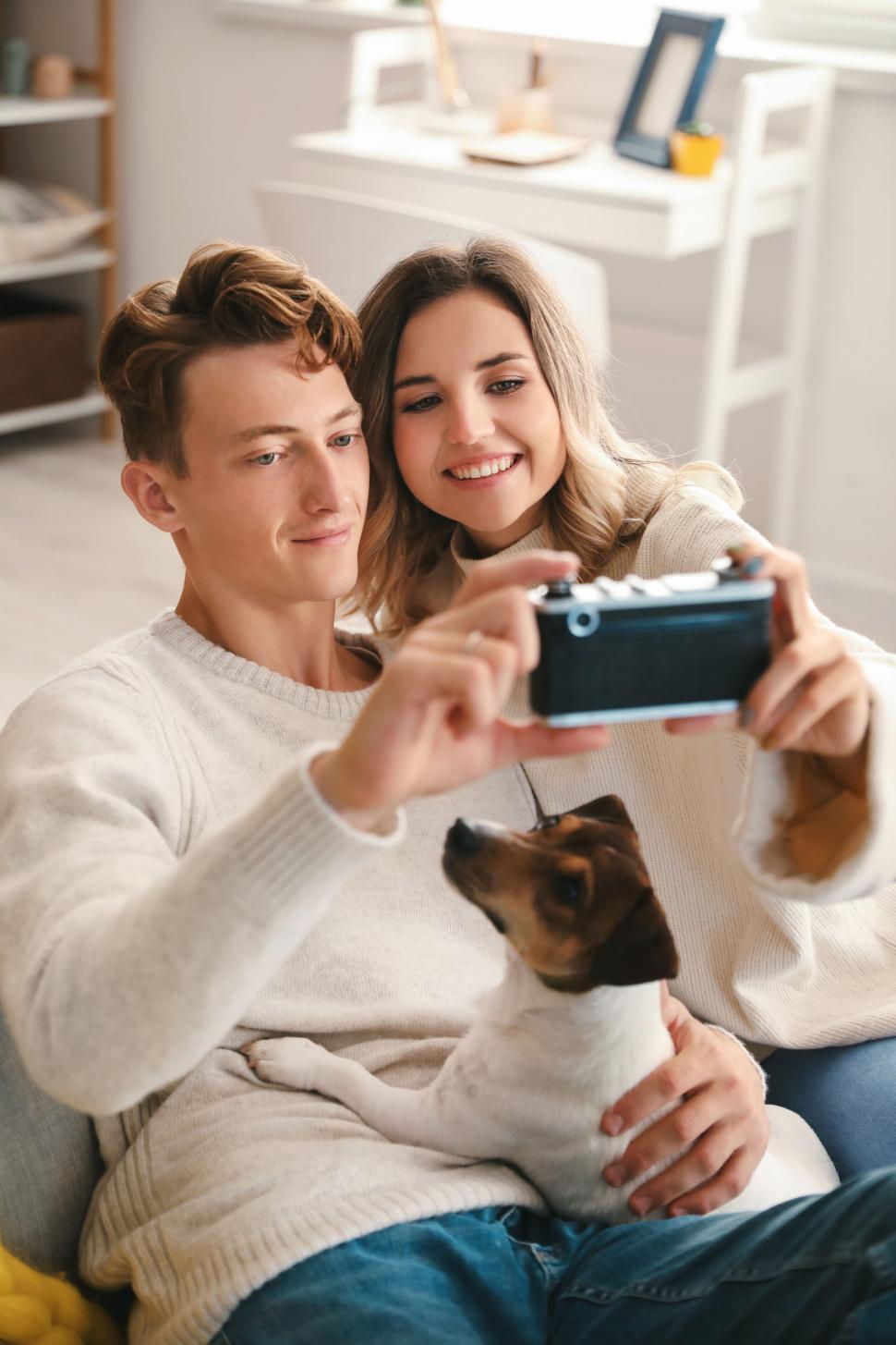 Free Image of Couple and dog taking a selfie in cozy living room, smiling faces. 