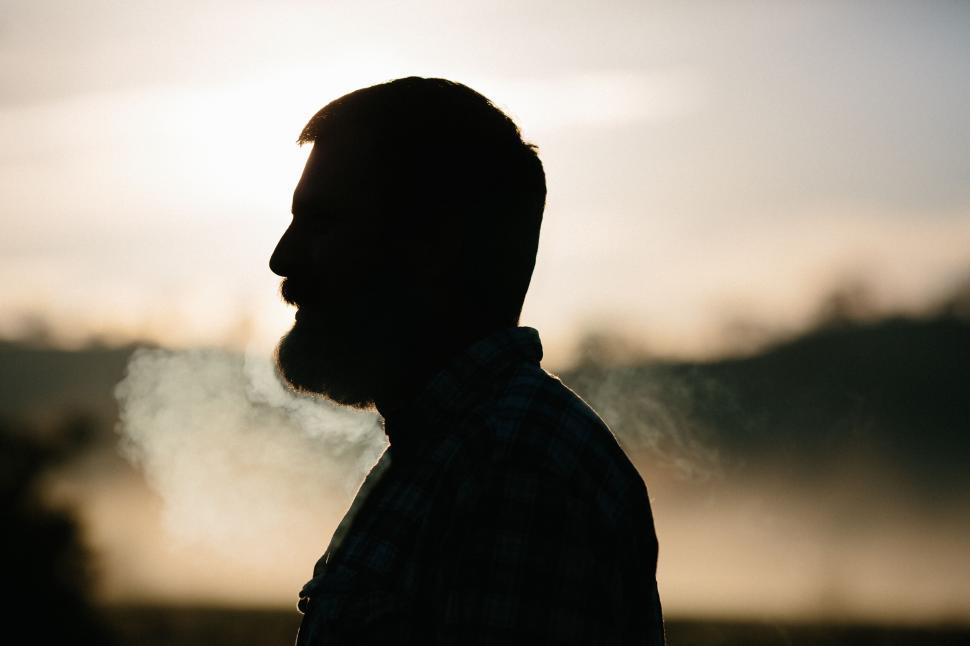 Free Image of Silhouette of a man smoking with a scenic sunset in the background 