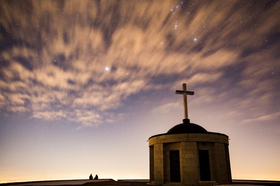 Free Image of Nighttime scene of two people near a cross-shaped monument. 
