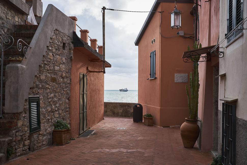 Free Image of Scenic seaside alley with colorful buildings and distant ship view 