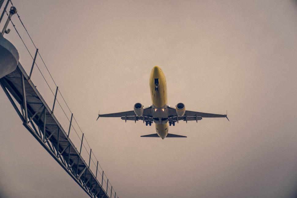 Free Image of Yellow airplane flying low over a modern airport runway. 