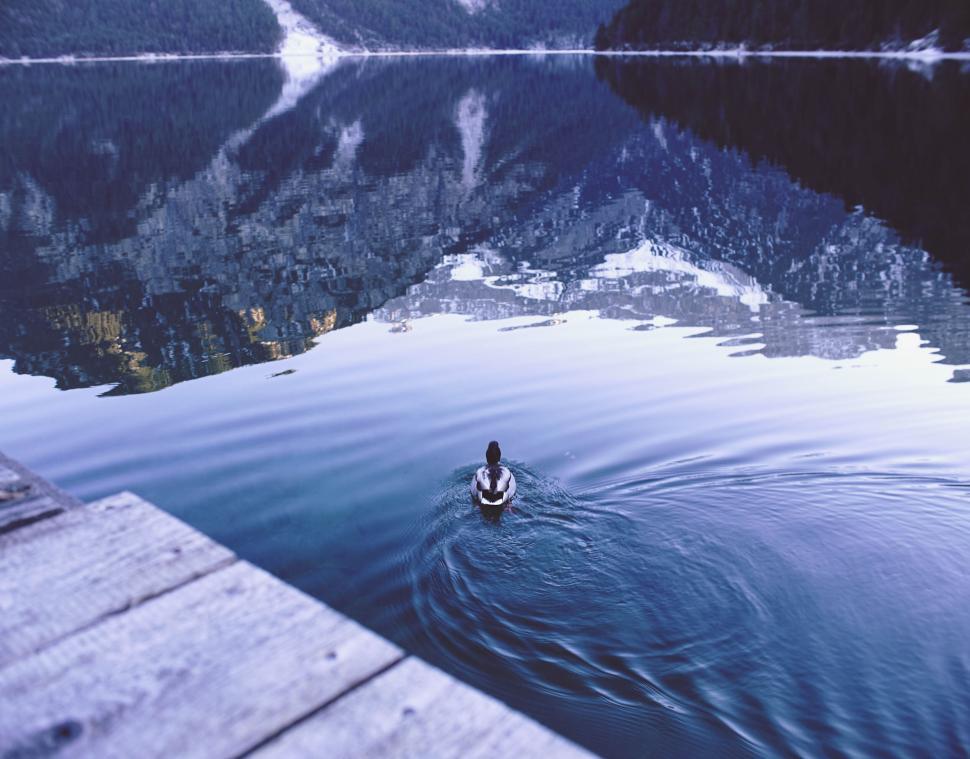 Free Image of Person swimming alone in a calm lake surrounded by mountains at dusk. 