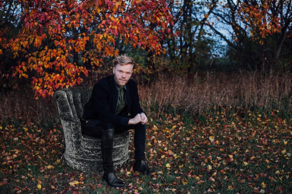Free Image of Man sitting on outdoor chair with autumn leaves and trees behind 