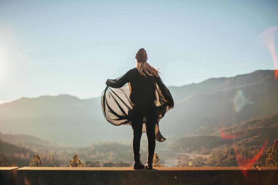 Free Image of Person on edge overlooking mountains at sunrise, arms outstretched. 