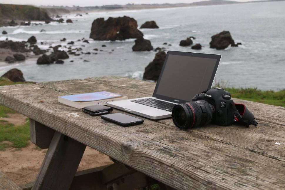 Free Image of Outdoor workspace with laptop, camera, and phones on wooden table 