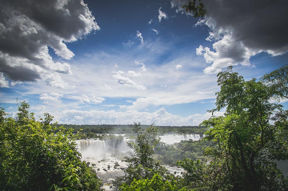 Free Image of Lush green forest with waterfalls and bright blue sky overhead 