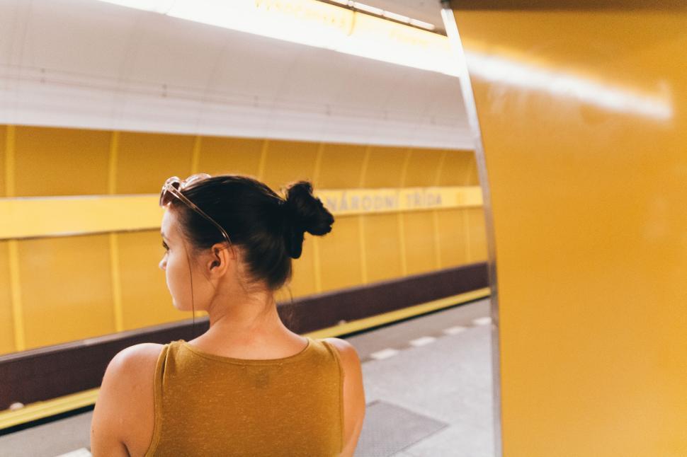 Free Image of Woman waiting at a subway station with a yellow themed design 