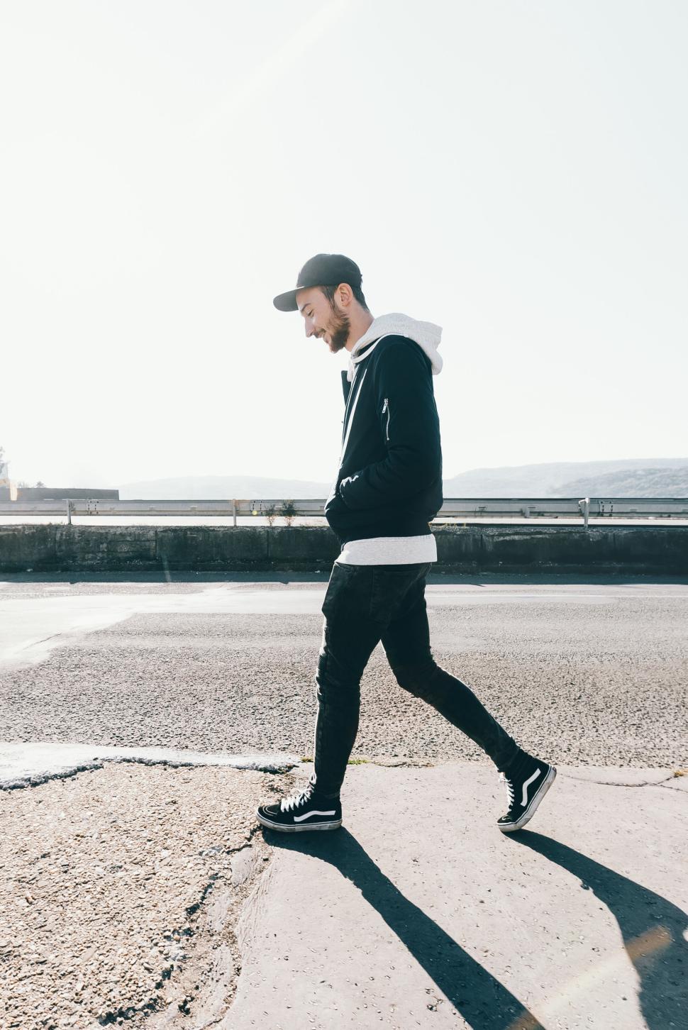 Free Image of Man walking on a sunny day with a cap and casual outfit outdoors 