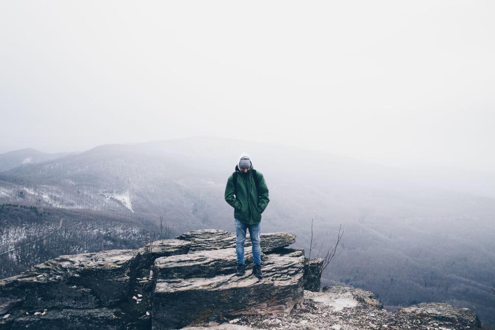 Free Image of A solitary figure standing on a rocky cliff with misty mountains 