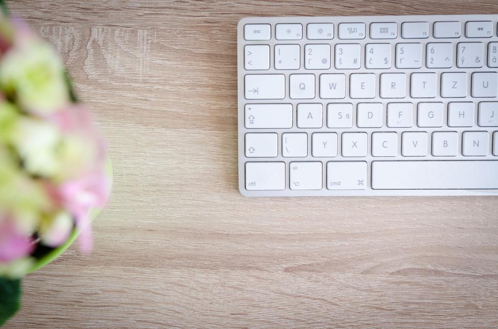 Free Image of White keyboard on wooden desk next to colorful blurred flowers 