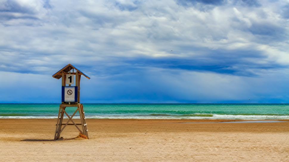 Free Image of Lifeguard house on a sandy beach under dramatic cloudy skies. 