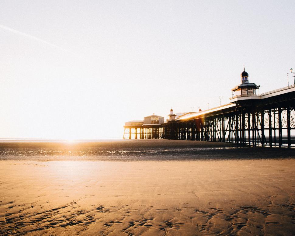 Free Image of Pier extending into the calm sea under the golden sunset light. 