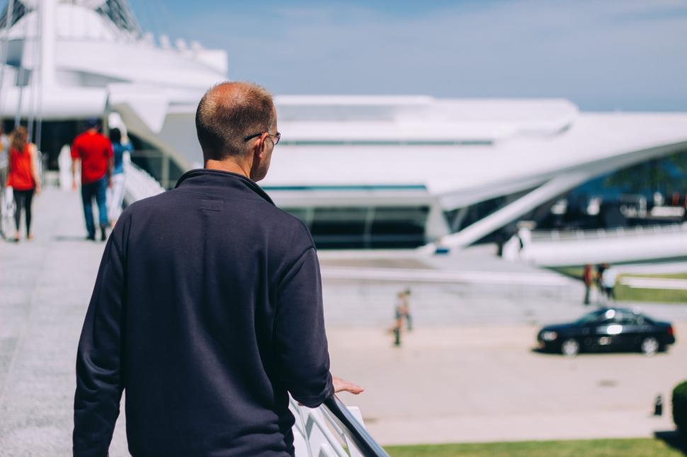 Free Image of Man with glasses on walkway in front of modern white building 