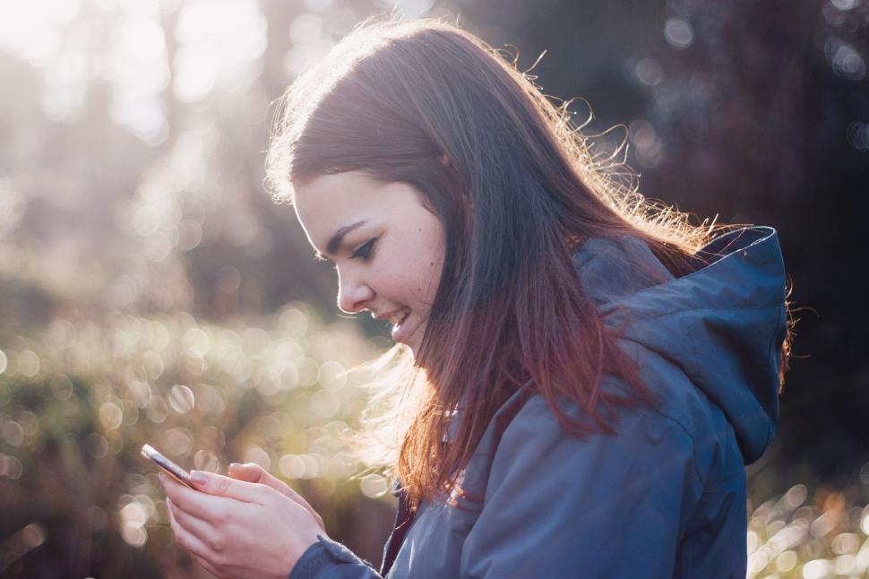 Free Image of Person using a smartphone outdoors wearing a jacket in sunny weather 